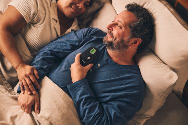 A well-rested couple lay in bed, the man holding the Inspire remote.